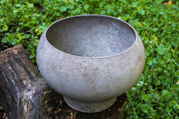 Outdated old large bell-shaped metal pot on wooden log