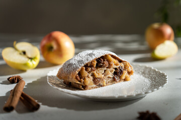 Apple pie - strudel or Apfelstrudel, sliced pie with apples, raisin and cinnamon on a gray table....
