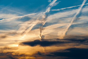 Morgen- oder Abendhimmel mit auf- oder untergehender von den Wolken verdeckter Sonne und Gewirr von sich kreuzenden, teilweise auflösenden Kondensstreifen