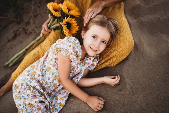 Girl lying on mom lap holding sunflowers at beach in summer