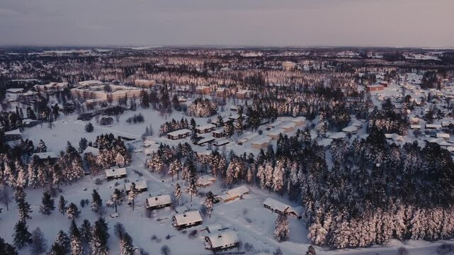 Peacefully flying over a neighborhood surrounded by trees and covered in snow during the sunset in north of Sweden