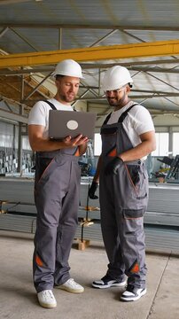 Two diverse workers with laptop in metal profile warehouse
