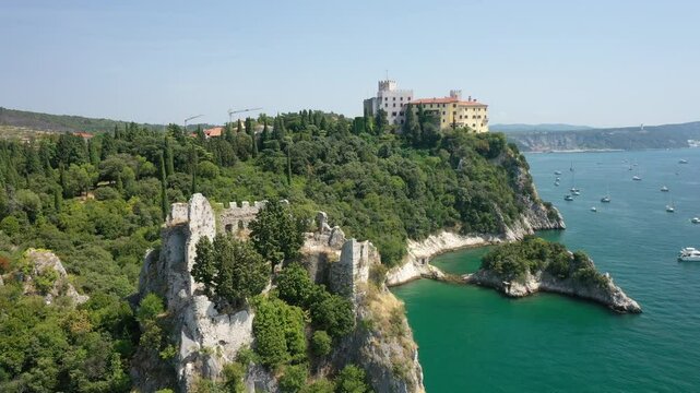Aerial Drone View of the Castle of Duino Near Trieste. Stunning aerial drone footage captures the majestic Castle of Duino perched on a rugged cliff overlooking the Adriatic Sea near Trieste, Italy. 