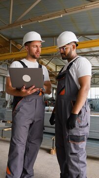 Caucasian foreman and Indian worker with laptop in warehouse metal profile