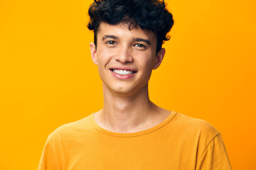 Smiling young man with curly hair wearing a yellow t shirt, standing against a vibrant yellow background, exuding positivity and joy, perfect for cheerful themes