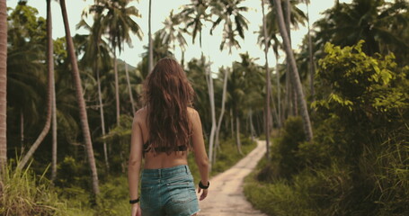 Young woman leisurely strolls through a lush tropical forest in thailand. Surrounded by towering palm trees and vibrant greenery