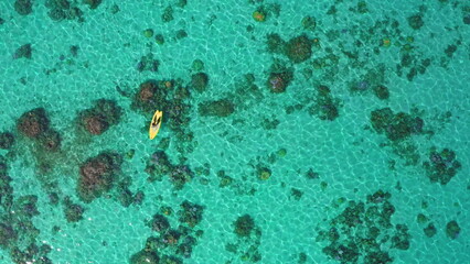 Mesmerizing aerial view captures a woman kayaking in turquoise waters above a vibrant coral reef in...