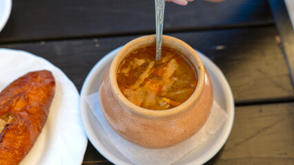A person is eating soup from a large bowl. The bowl is on a white plate and is filled with a thick, brown soup. A spoon is being used to eat the soup
