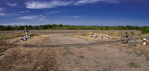 Obraz premium Panorama. Narrow-gauge railway, crossing. Cycling along the outskirts.Field entourage. Bright sun at midday.Railway on the outskirts.Narrow gauge.