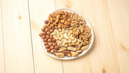 A plate of nuts and seeds on a wooden table. The plate is white and has a variety of nuts and seeds on it