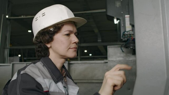 Medium closeup of mature female factory worker adjusting settings of industrial machine