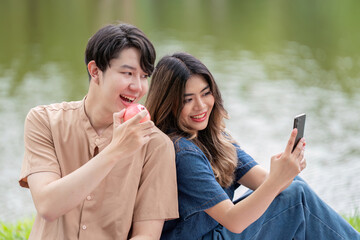 Asian couple sharing joyful selfie moment during lakeside picnic