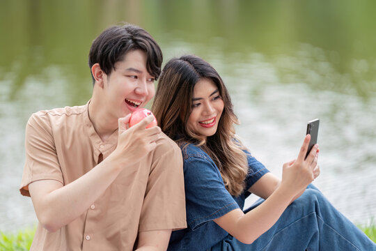 Asian couple sharing joyful selfie moment during lakeside picnic