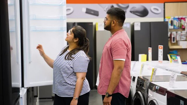 Young Indian couple is viewing fridge in home appliances store