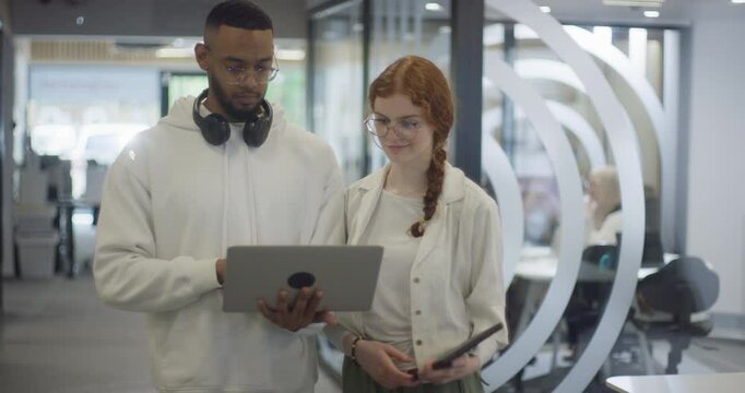 A woman with vibrant orange hair and an African-American business man work together in a modern office, collaboratively solving various business challenges, illustrating diversity, innovation, and