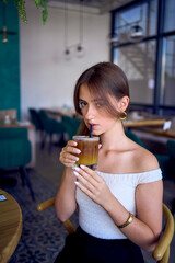 16-year-old teenage girl in old money style clothes drinks bumble coffee with an orange in a fancy restaurant