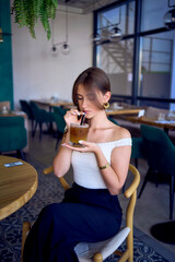 16-year-old teenage girl in old money style clothes drinks bumble coffee with an orange in a fancy restaurant