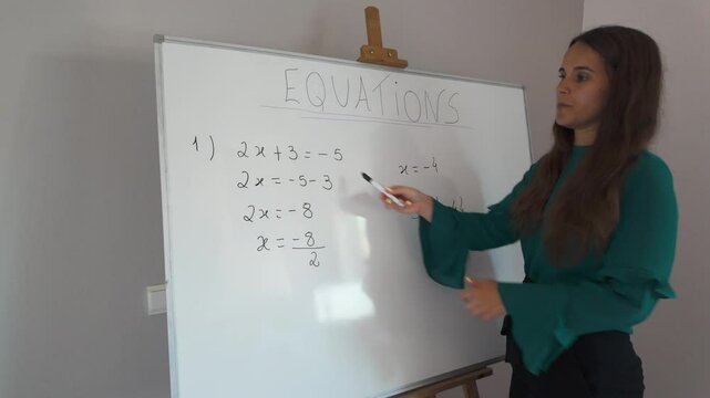 Woman teaching equations on a whiteboard in a classroom setting