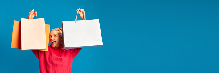 Happy and excited young woman raising colorful shopping bags above head against blue studio...