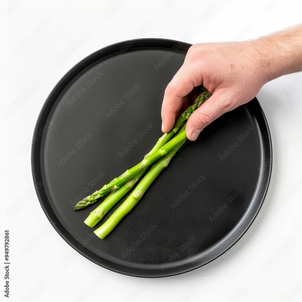 Poster Hand placing fresh asparagus spears on a black plate.