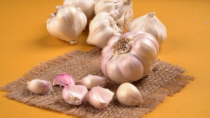 Organic Garlic. Fresh Garlic Cloves and Garlic bulb in wooden basket on yellow background with Pile of garlic or spice. Concept of spices for healthy cooking.