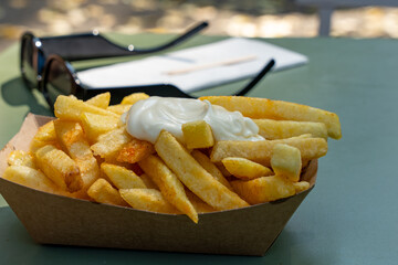 A tray of french fries with a white sauce on top. The fries are in a paper basket and are sitting...