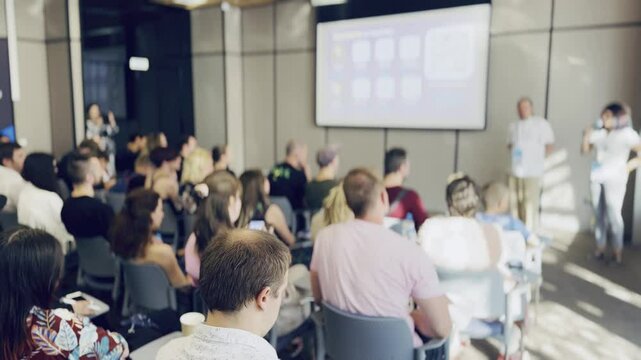 Group of diverse individuals attending a business conference, focused on a presentation displayed on a large projector screen. Engaging and collaborative learning environment.
