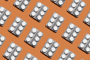 Pattern of blister pack with six round white tablets on orange background, creating a visually striking geometric layout. Creative pills concept