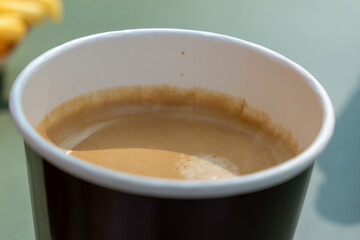 There is a cup of coffee on the table. The coffee is brown in color and has a creamy texture. The cup is made of paper.