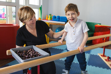 Young boy with movement disorders smiles while participating in physical rehabilitation, supported...