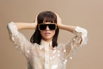 Woman with sunglasses raises her hands over her head against a beige backdrop, exuding a casual, stylish vibe with a touch of confidence and fashionforward flair, perfect for lifestyle and fashion