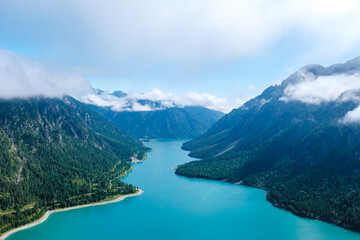 Obraz premium Majestic views of Plansee in Austria with turquoise waters and misty mountains on a sunny day