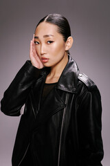 Asian woman, fashion, black leather jacket, hand to face a stylish asian woman poses in a black leather jacket while gracefully holding her hand to her face