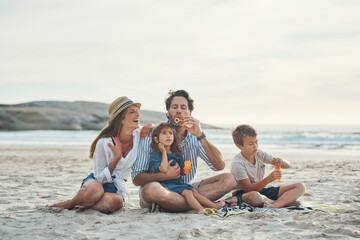 Happy, family and relax with bubbles on beach for playing, summer fun and seaside adventure on...