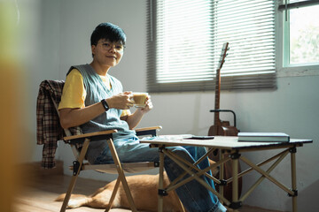 Fototapeta premium Asian embracing LGBTQ identities, smile warmly at the camera, enjoying coffee and guitar near window capturing a joyful and inclusive moment of their lifestyle at home.