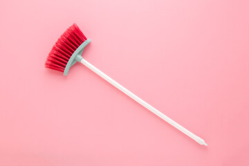 New red broom with white plastic stick for child on light pink table background. Pastel color....