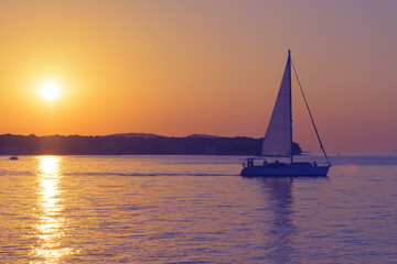Sailboat departing at sunset. Romantic scene with a silhouetted boat sailing to open sea against a vivid colorful sunset in Croatia. Tourism, travel and optimism concepts.
