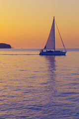 Sailboat leaving the Croatian coast after sunset. Romantic scene with a silhouetted boat sailing to open sea against a vivid colorful sunset in Croatia. Tourism, travel and optimism concepts.