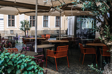 Outdoor cafe with empty tables and chairs, shaded patio, historic European architecture, cozy atmosphere, urban dining, street cafe.