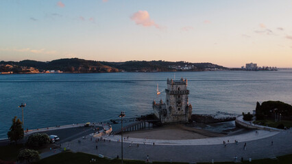 An aerial drone image of the iconic Bel&eacute;m Tower in Lisbon, Portugal, set against the serene backdrop of the Tagus River at sunset. Lisbon