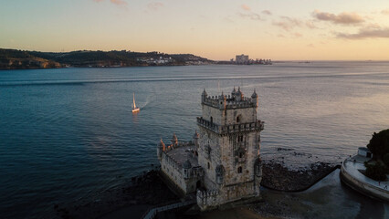Obraz premium An aerial drone image of the iconic Belém Tower in Lisbon, Portugal, set against the serene backdrop of the Tagus River at sunset. Lisbon