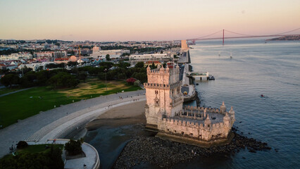 An aerial drone image of the iconic Bel&eacute;m Tower in Lisbon, Portugal, set against the serene backdrop of the Tagus River at sunset. Lisbon