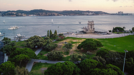 An aerial drone image of the iconic Belém Tower in Lisbon, Portugal, set against the serene backdrop of the Tagus River at sunset. Lisbon