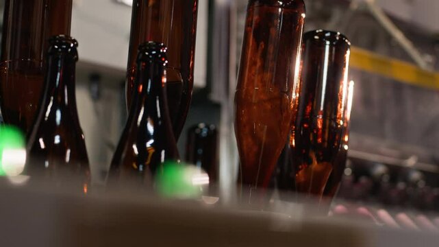Conveyor belt with brown glass bottles set up upside down on working filling machine at cider production factory