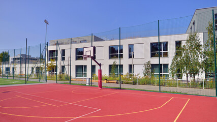 Fototapeta premium Schoolyard with basketball court and school building exterior in the sunny day. 