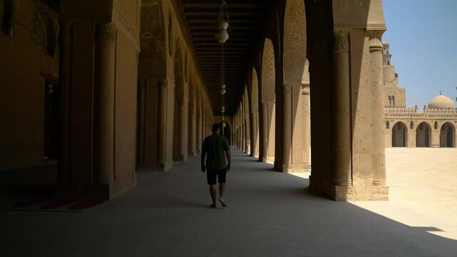 Revealed Man Walking At Arched Hallway Of Ibn Tulun Mosque In Cairo, Egypt. Tilt-down Shot