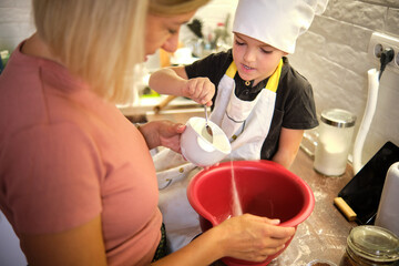 A child helps an adult mix ingredients in a red bowl during a fun cooking session in a cozy kitchen