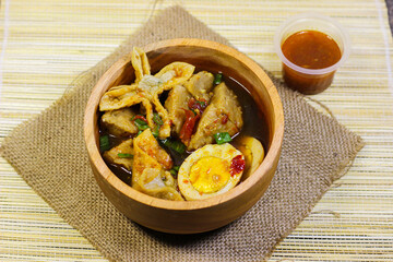 Meatballs, eggs and dumplings served with spicy sauce in a wooden bowl