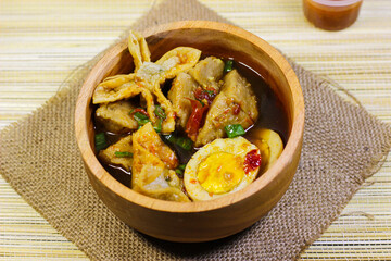 Meatballs, eggs and dumplings served with spicy sauce in a wooden bowl