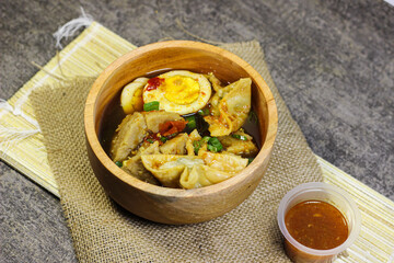 Meatballs, eggs and dumplings served with spicy sauce in a wooden bowl